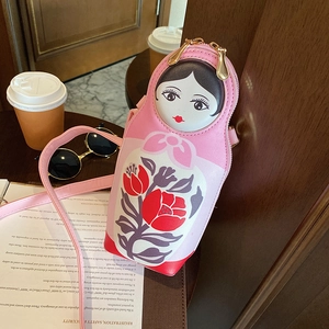 Pink Matryoshka doll-shaped PU crossbody bag with floral prints on a wooden table