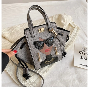 Detail of grey crocodile pattern handbag with lady illustration and gold twist lock