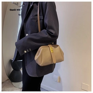 Detail of a beige vintage shell bag with gold twist lock worn by a model in a suit
