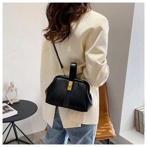 Detail of a black pebbled leather shell bag featuring a gold metal lock and carry handle