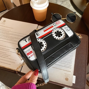 Detail of retro cassette tape shaped crossbody bag with gold chain strap on cafe table