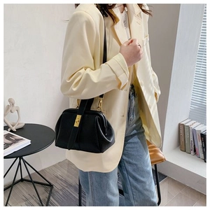 Detail of black leather doctor bag with gold twist lock on a minimalist blazer outfit