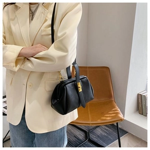 Side view of black lychee grain leather doctor bag with gold clasp shown on a model