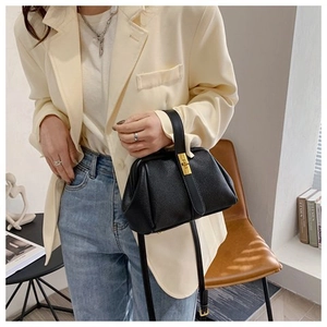 Detail of black pebbled leather shell bag with gold clasp shown on a crossbody model