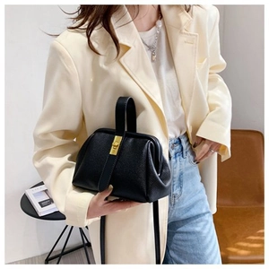 Detail of black lychee grain leather shell bag with gold metal clasp on model