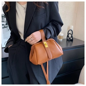 Detail of a brown lychee pattern leather handbag with golden clasp and black suit styling