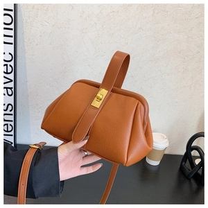 Detailed close-up of brown litchi grain leather shell bag with gold lock and shoulder strap