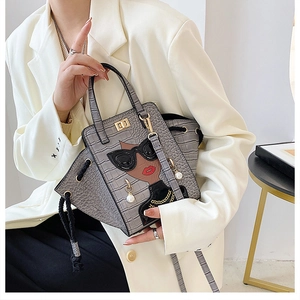 Detail of grey crocodile pattern handbag featuring a cartoon girl motif and gold clasp
