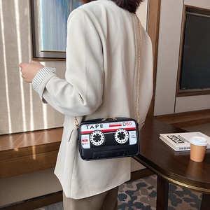 Detail view of a retro cassette tape clutch bag with gold chain strap worn by a model