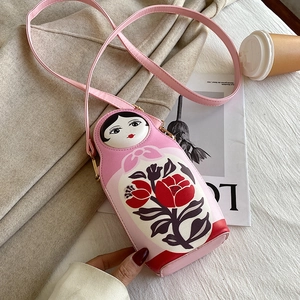 Pink nesting doll crossbody bag in PU leather styled on an elegant light coat background