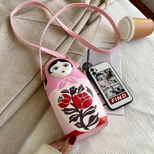 Detailed view of pink Russian nesting doll crossbody bag on a warm fabric texture