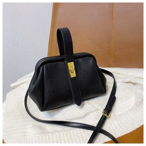 Detail of black lychee grain leather shell bag with golden metal buckle and top handle