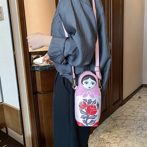 Close-up of the Russian doll shaped PU crossbody bag worn by a model in a modern home setting