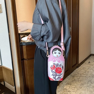 Detail of pink Russian doll crossbody bag with floral patterns on a model's shoulder