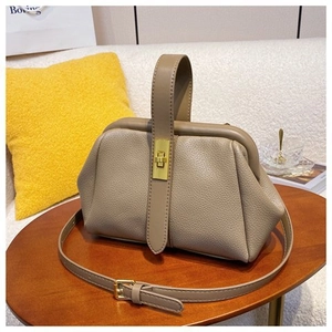Detail of khaki leather doctor bag with litchi texture and gold twist lock on wooden table