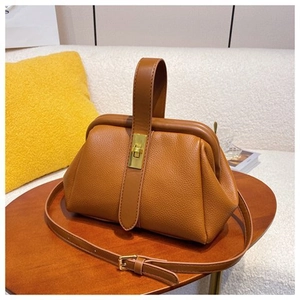 Detail of caramel lychee grain leather shell bag with gold metal twist lock on wood table