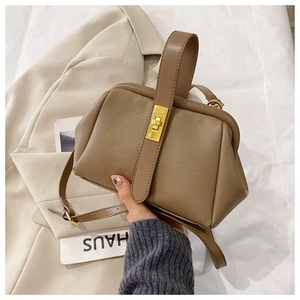 Detail of tan pebble leather shell bag with gold clasp and elegant handheld strap
