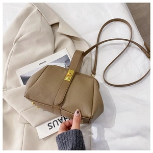 Detail of brown vintage shell bag with gold clasp and leather strap on beige blazer