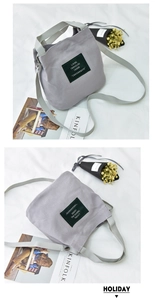 Close-up of grey canvas bucket bag with green letter patch and woven straps detail