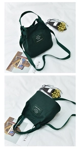 Detail view of dark green canvas bucket bag showing top handle, strap and metal closure