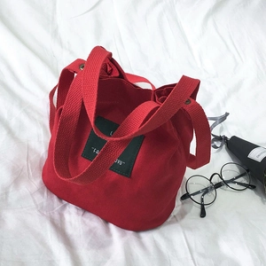 Mini red canvas bucket bag for women with decorative patch on a soft fabric background