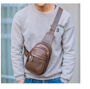 Detail of dark brown leather sling bag featuring dual zip pockets and pebble texture