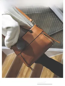 Detail view of brown leather tote with double zipper decor and grey pompom keychain charm
