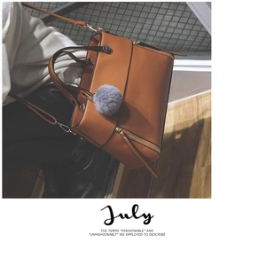 Close-up of caramel faux leather tote bag with grey fur ball charm on wooden stairs