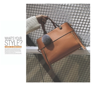 Detail of caramel leather tote bag featuring stylish gray pompom and dual side zippers