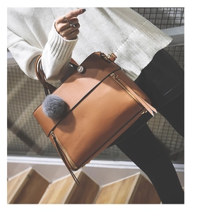 Detail of brown faux leather tote bag with gold zippers and grey fur ball accessory