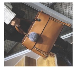 Close-up of caramel tote bag featuring side zippers and a soft grey pompom charm detail