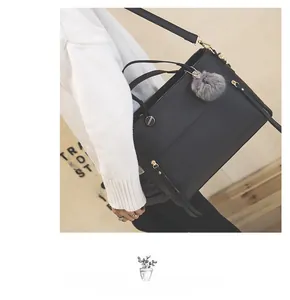 Detail of black matte leather tote bag with gold zipper and gray faux fur pom-pom charm