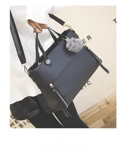 Detail showing black textured leather tote with metal zipper and grey pom-pom charm