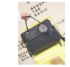 Detail of black tote bag with gold zipper and gray faux fur ball charm on yellow chair