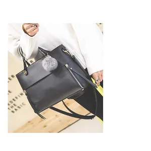 Detail of black leather tote bag featuring a decorative grey faux fur pompom and strap