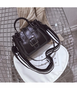 Detail of black glossy leather handbag with wide striped strap and silver buckle