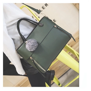 Detail of dark green tote bag featuring double zippers, plush charm, and black handles