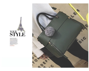 Detail of dark green tote bag featuring luxury gold hardware and a grey faux fur pom pom
