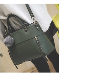 Detail of dark green tote bag with decorative zippers, metal buckles and gray pompom charm