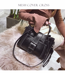 Detail of black glossy tote bag with white contrast stitching and square metal buckle