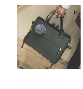 Detail of dark green tote bag with zipper decor and a grey plush pom-pom accessory