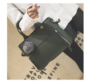 Detail of dark green tote bag with grey fur pompom charm and metal zipper buckle
