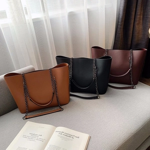 Three-piece tote bag set in brown black and burgundy with chain straps on a sofa