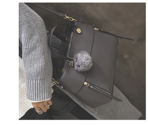 Detailed view of dark grey matte leather tote bag with fluffy ball charm and gold hardware