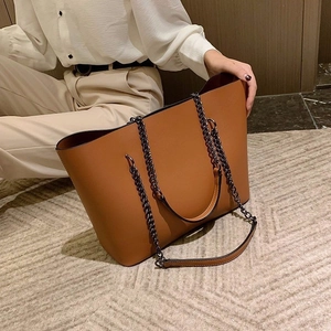 Caramel brown leather tote bag with metal chain strap shown in a minimalist home setting