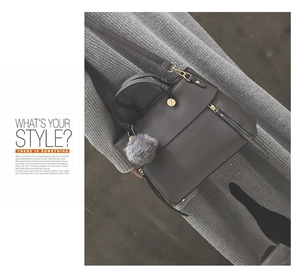 Detail of dark grey tote bag featuring a decorative fur ball charm and side zippers