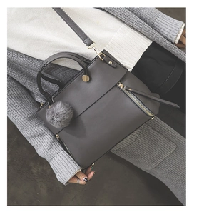 Detail of grey tote bag with faux fur charm, adjustable strap and metallic hardware accents