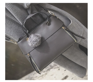 Detail of dark grey leather tote bag with gold zippers and grey pompom on grey sweater