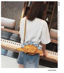 Detail shot of a yellow dinosaur crossbody bag with blue fins and a thin shoulder strap