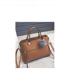 Caramel textured leather tote bag with gray faux fur pom-pom detail on concrete floor
